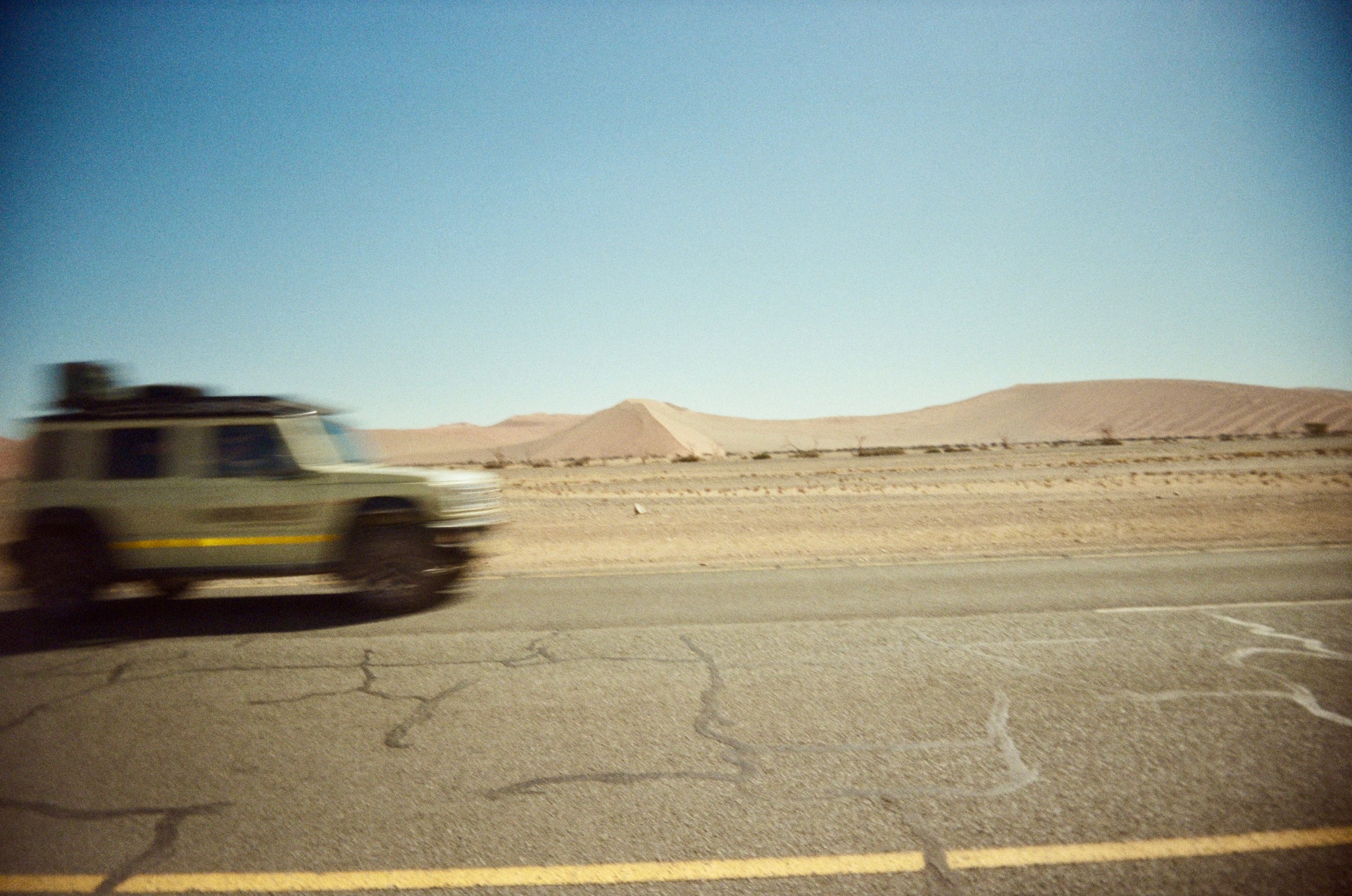 Motion-blurred vehicle passing dunes on a desert road, shot on 35mm film